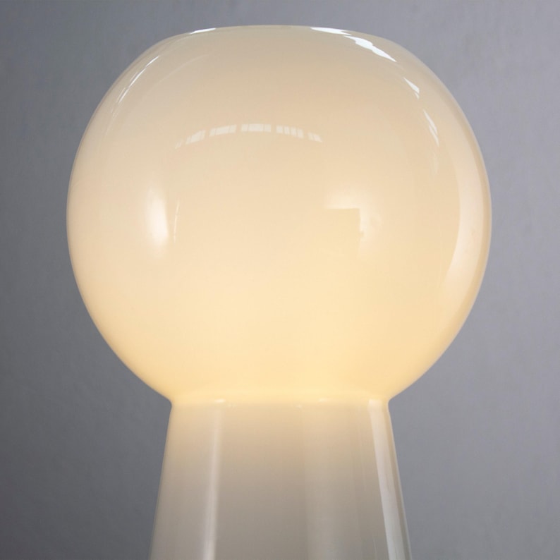 A white, round lamp with a reflective surface, standing against a gray background.