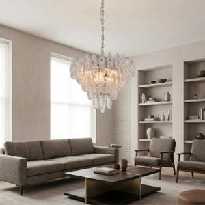 a modern living room with a large crystal chandelier hanging from the ceiling, casting a warm glow throughout the space. The room is furnished with a gray sofa, two armchairs, and a coffee table. The walls are painted in a light color, and the room is well-lit by natural light coming through a window.
