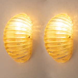 May include: A pair of wall sconces with ribbed glass shades. The shades are a light yellow color and are illuminated from within.