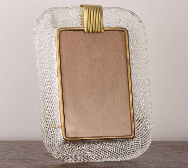 May include: A clear glass picture frame with a textured surface and a gold metal trim. The frame has a rectangular opening for a photo.