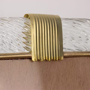 May include: Close-up of a gold metal trim on a clear glass lampshade. The trim has a wavy edge and a ribbed texture.