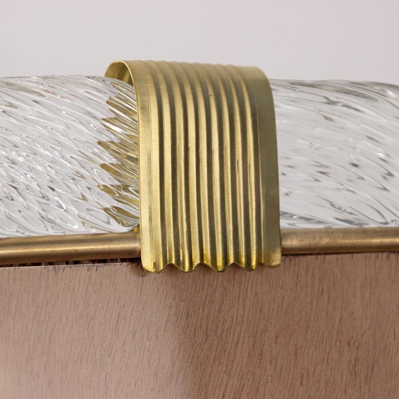 May include: Close-up of a gold metal trim on a clear glass lampshade. The trim has a wavy edge and a ribbed texture.