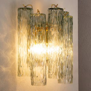 May include: A wall-mounted light fixture with five frosted glass shades. The shades are textured and have a rippled effect. The fixture is made of brass and has a modern design.