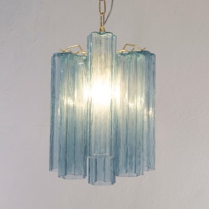 May include: A vintage-style chandelier with a light blue glass design. The fixture has a series of vertical, textured glass panels, suspended from a gold-colored chain and decorative accents. The light shines through the glass, creating a soft glow.