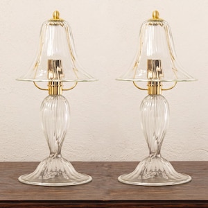Two clear glass lamps with gold bases, placed side by side on a wooden surface against a white background.