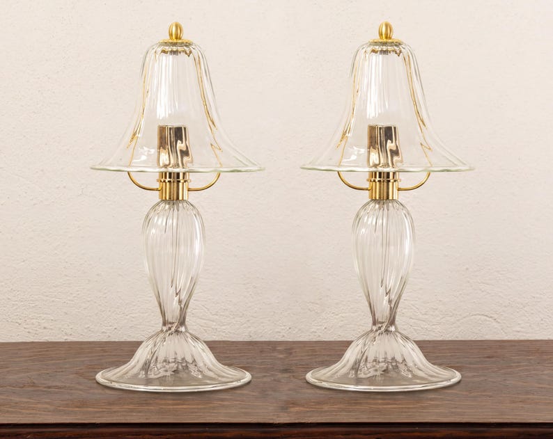Two clear glass lamps with gold bases, placed side by side on a wooden surface against a white background.