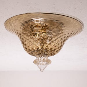 May include: A ceiling light fixture featuring a textured, amber-toned glass shade. The shade has a dimpled pattern and a clear glass decorative element. The light fixture is designed for ceiling mounting, offering a warm, inviting glow.
