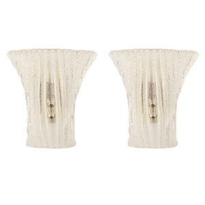 May include: A pair of clear glass wall sconces with a textured, ribbed design. The sconces have a simple, modern style and would add a touch of elegance to any room.