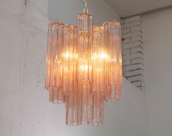 May include: A vintage-style chandelier with a tiered design. The light fixture features numerous pink glass tubes, creating a textured appearance. The chandelier is suspended from a gold-colored chain, and the light shines through the glass.