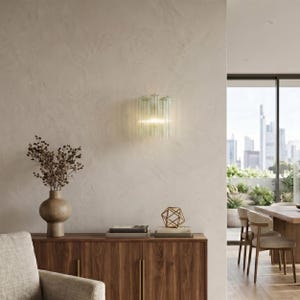 a modern living room with a wooden cabinet, a vase with dried flowers, and a geometric sculpture on a wooden surface. The room has a large window overlooking a city skyline, and the overall color scheme is neutral, with a touch of green from the sculpture.