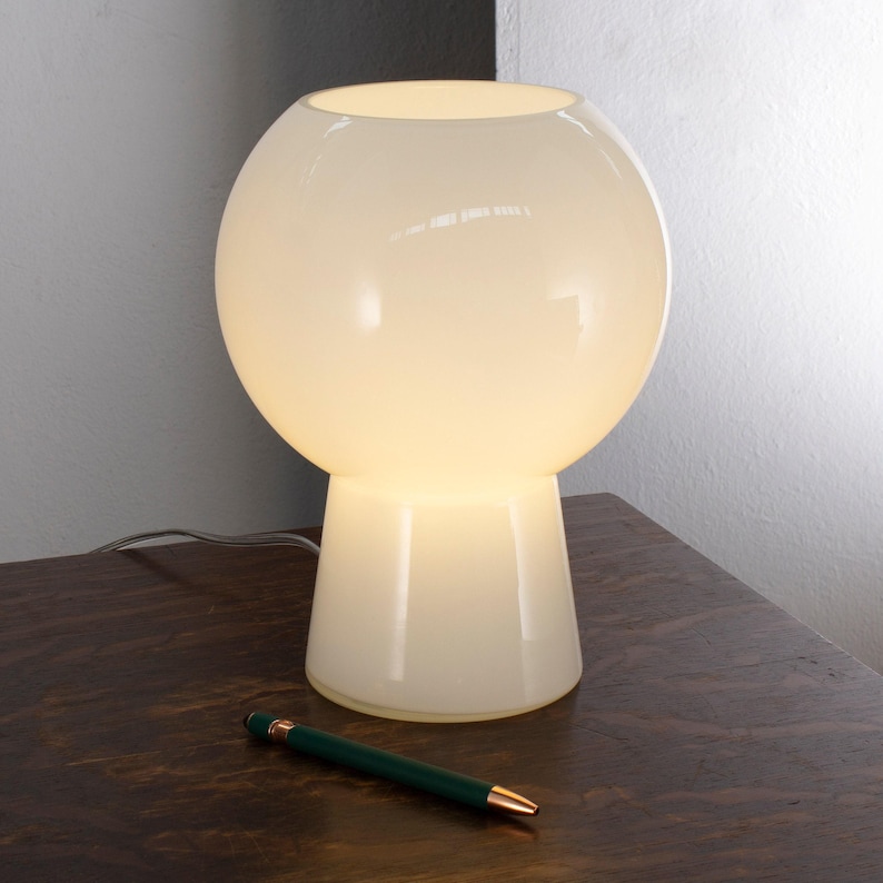 A white lamp with a round base and a green pen on a wooden surface.