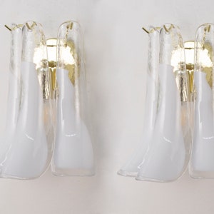 Könnte beinhalten: Zwei goldene Wandleuchten mit weißen Glasschirmen. Die Schirme sind Blütenförmig und haben eine strukturierte Oberfläche.