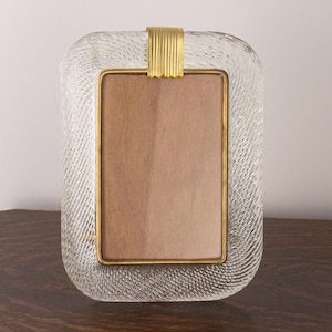 May include: A clear glass picture frame with a gold metal trim and a textured surface. The frame has a rectangular shape with rounded corners.