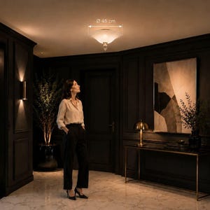 A woman stands in a dimly lit hallway, gazing upwards at a ceiling light fixture.