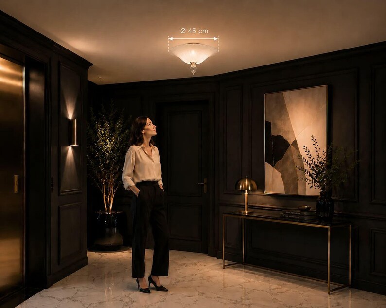 A woman stands in a dimly lit hallway, gazing upwards at a ceiling light fixture.