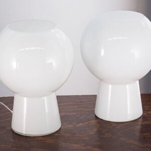 Two white, round table lamps with a modern, minimalist design sit on a wooden surface.