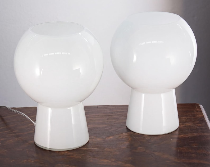 Two white, round table lamps with a modern, minimalist design sit on a wooden surface.