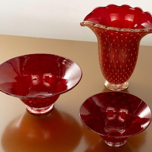 Può includere: Tre pezzi di decorazioni per la casa in vetro rosso. Il set comprende due ciotole e un vaso con bordo a balze. Il vaso e una ciotola hanno una base trasparente. Il vaso ha una superficie strutturata con piccole bolle incorporate.
