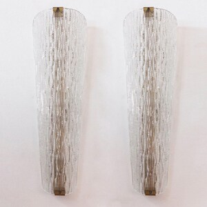 Two tall, clear glass wall sconces with a textured, woven pattern on the surface, mounted on a white wall.