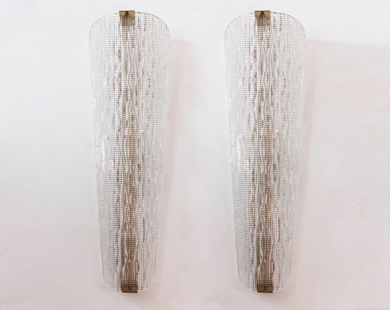 Two tall, clear glass wall sconces with a textured, woven pattern on the surface, mounted on a white wall.