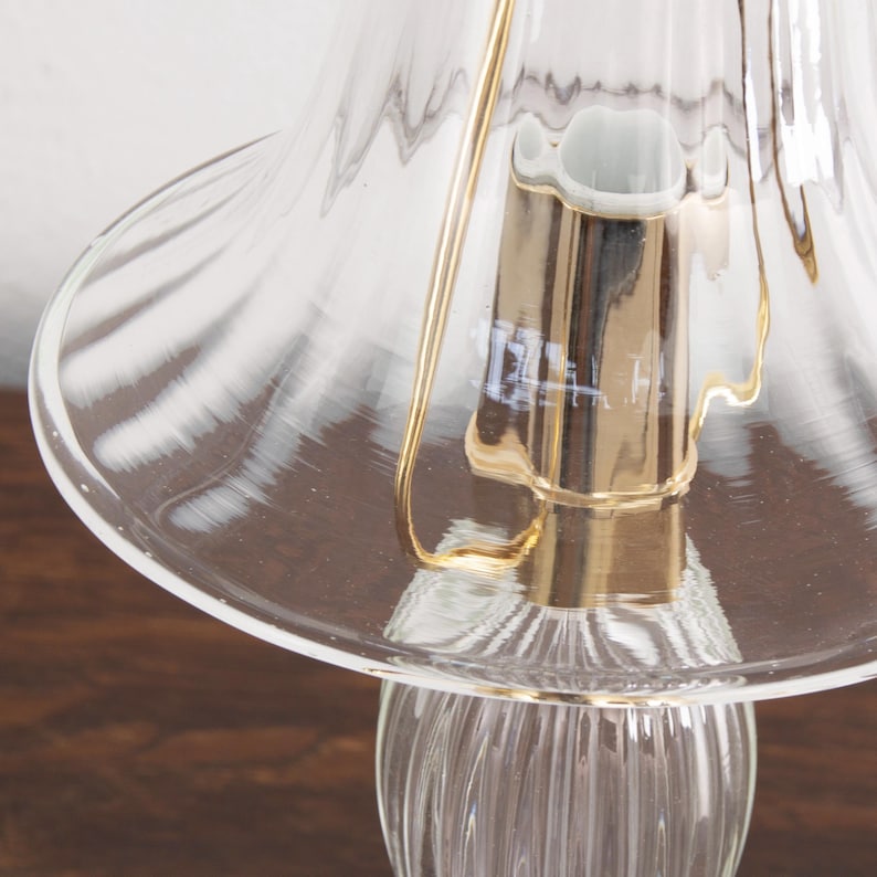 A close-up view of a glass lampshade with a gold-colored metal base, placed on a wooden surface.