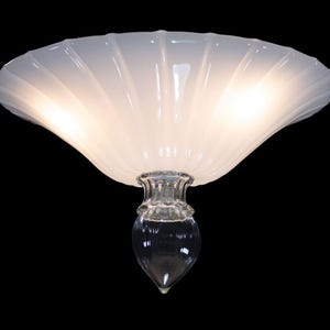A white, scalloped-edge lamp shade with a clear glass base and a single light bulb.