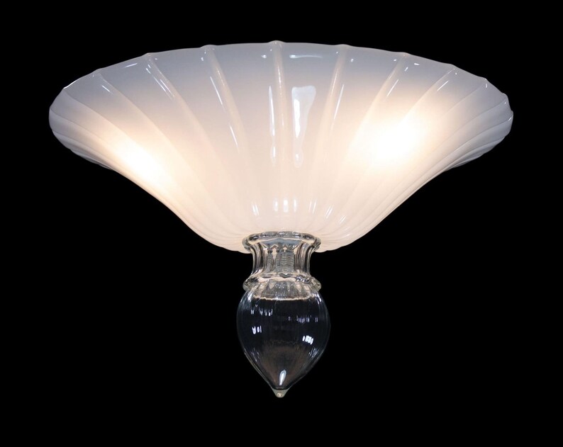A white, scalloped-edge lamp shade with a clear glass base and a single light bulb.
