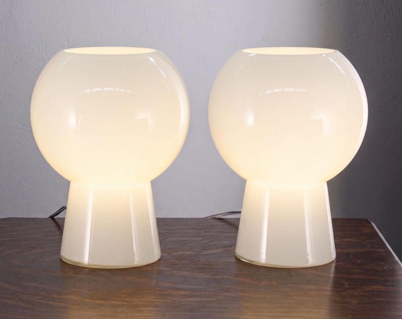 Two white, round table lamps with a simple, minimalist design sit side by side on a wooden surface.