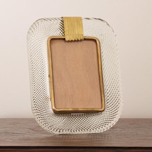 May include: A clear glass picture frame with a textured surface and a gold metal trim. The frame has a rectangular opening for a photo.