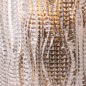 a close-up view of a textured, glass surface with a repeating pattern of small, square-shaped lines and curves. The glass appears to be made of a clear material, possibly glass or a similar transparent material, with a metallic or textured finish. The image does not contain any discernible objects or actions, and the focus is on the intricate and visually interesting pattern created by the glass surface.