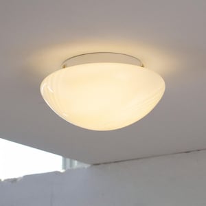 Può includere: Una plafoniera a incasso con un paralume in vetro bianco traslucido a forma di ciotola con sottili motivi a vortice. Il paralume in vetro è fissato a una base circolare bianca tramite piccoli elementi di fissaggio metallici.