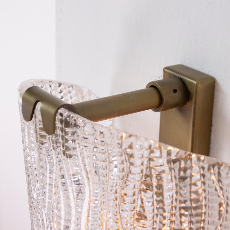 a wall-mounted light fixture with a clear, textured glass shade. The fixture has a brass-colored metal bracket and is attached to a white wall.