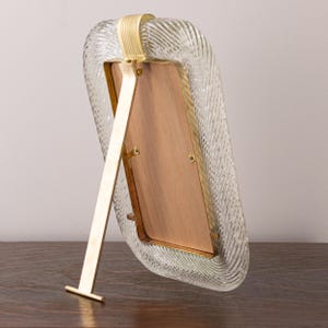 May include: A gold-toned picture frame with a clear, textured glass front. The frame has a kickstand on the back to stand upright.