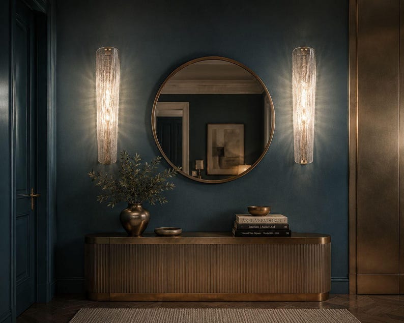 a modern and stylish interior design with a large round mirror, two wall sconces, a wooden console table, and a vase of greenery.