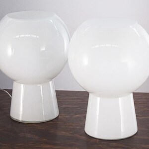 Two white, round table lamps with a simple, minimalist design sit on a wooden surface.