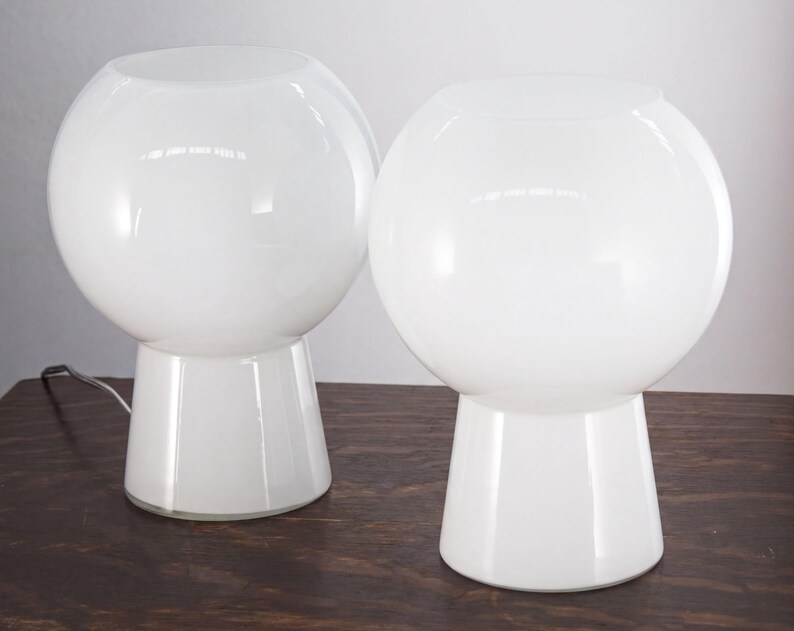 Two white, round table lamps with a simple, minimalist design sit on a wooden surface.