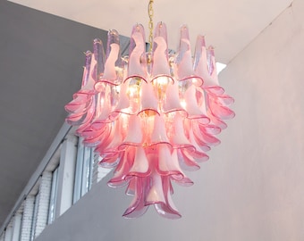 May include: A pink and white chandelier with a floral design. The light fixture is suspended from a gold chain and features multiple tiers of petal-shaped glass elements. The light bulbs are visible within the fixture.
