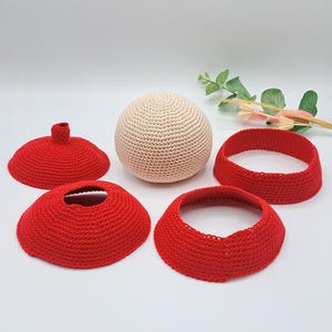 May include: A set of crocheted items in red and cream. The set includes a sphere, a ring, and two bowl-shaped pieces.