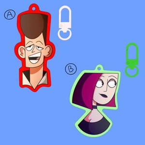 May include: Two cartoon character keychains. The first keychain is red and features a cartoon man with brown hair and a white shirt. The second keychain is green and features a cartoon woman with pink hair and a black shirt.