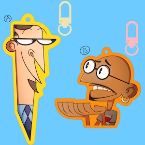 May include: Two cartoon character keychains. The first keychain is yellow and features a man with a long nose, glasses, and a blue and white checkered tie. The second keychain is orange and features a man with brown skin, glasses, and a red and white striped shirt.