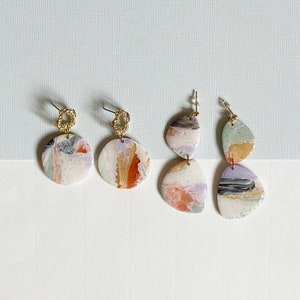 Peut inclure: Trois paires de boucles d'oreilles abstraites colorées avec des accents dorés. Les boucles d'oreilles sont en céramique et ont un design unique peint à la main.