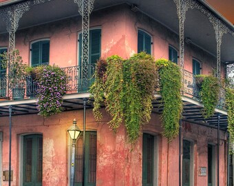 May include: A pink building with a wrought iron balcony and green shutters. The building has a balcony on each floor and is covered in vines.