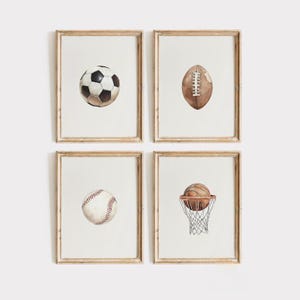 Puede incluir: Cuatro impresiones enmarcadas en acuarela con equipamiento deportivo. Se representan un balón de fútbol, un balón de fútbol americano, una pelota de béisbol y un balón de baloncesto en una canasta. Los marcos son de color madera clara y el fondo es blanco.