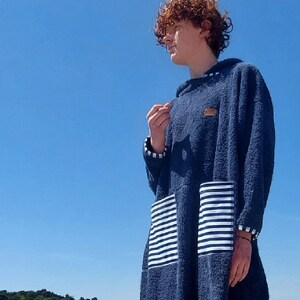 May include: A person wearing a blue hooded towel with white stripes on the pocket. The towel is made of a soft, absorbent material and is perfect for drying off after a swim.