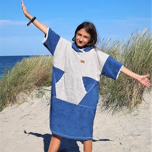May include: A young person wearing a blue and white hooded towel with a large pocket on the front. The towel is made of soft, absorbent material and is perfect for drying off after a swim or a day at the beach.