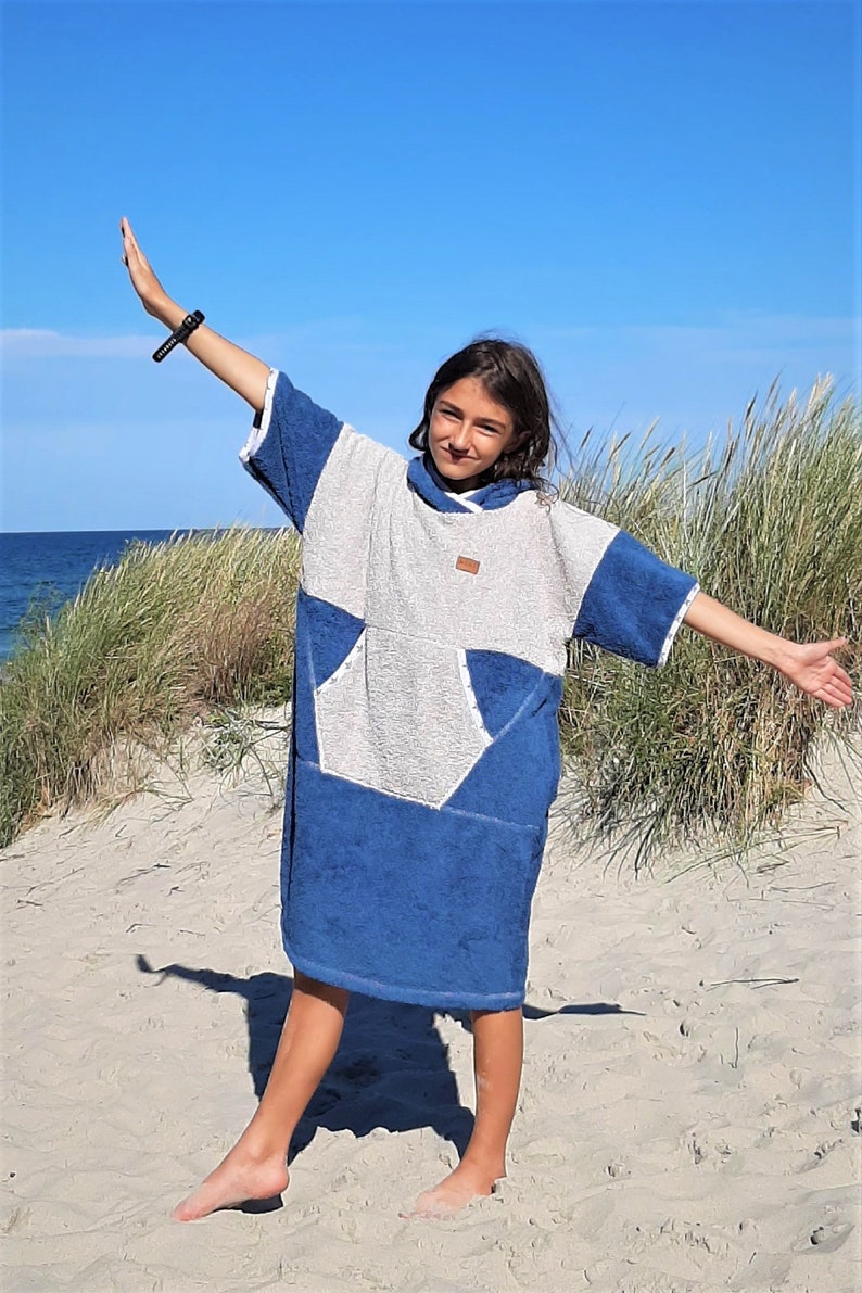 May include: A young person wearing a blue and white hooded towel with a large pocket on the front. The towel is made of soft, absorbent material and is perfect for drying off after a swim or a day at the beach.