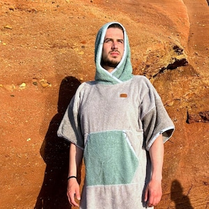 Könnte beinhalten: Ein Kapuzenbademantel in Grau und Grün mit einer großen Tasche auf der Vorderseite. Der Bademantel ist aus weichem, saugfähigem Material und perfekt zum Trocknen nach dem Schwimmen oder Duschen.