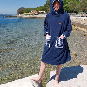 May include: A navy blue hooded towel robe with white stripes on the pockets. The robe is made of a soft, absorbent material and is perfect for drying off after a swim.