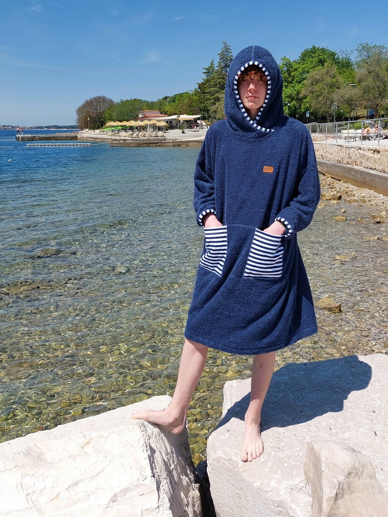 May include: A navy blue hooded towel robe with white stripes on the pockets. The robe is made of a soft, absorbent material and is perfect for drying off after a swim.