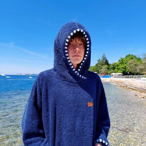 May include: A navy blue hooded towel with white stripes on the hood and pockets. The towel has a brown patch with the word "ONE" on it.